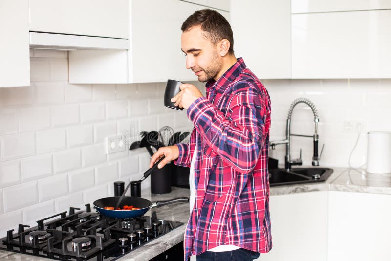 Single young handsome man alone at home puts olive vegetable oil in frying pan royalty free stock photography