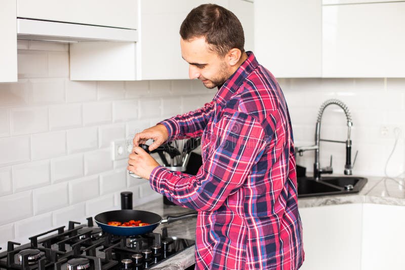 Single young handsome man alone at home puts olive vegetable oil in frying pan royalty free stock image