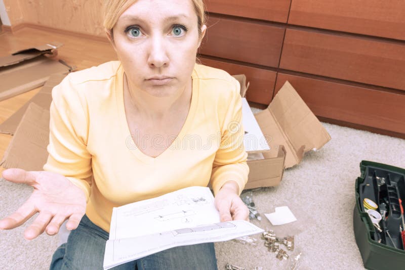 Single young woman assembling pieces of new furniture and reading the instruction, she is confused, open boxes with furniture