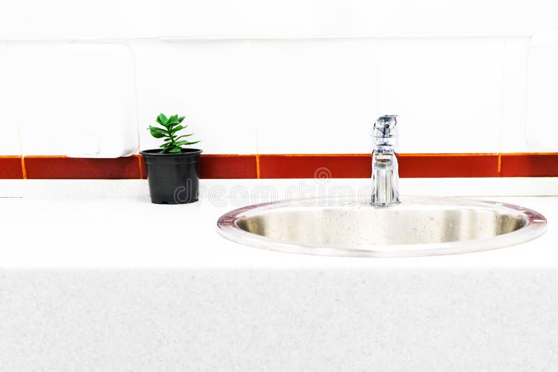 The sink in the bathroom on the background of bright tiles with a bright stripe, the design of a flower in a pot stock photo The sink in the bathroom on the background of bright tiles with a bright stripe, the design of a flower in a pot stock photo
