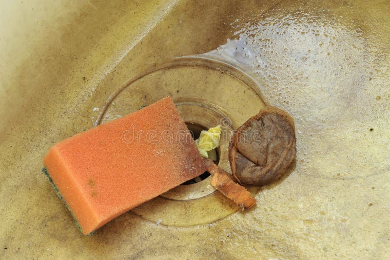 Stained and dirty unhygienic kitchen sink with wash sponge, food waste and used tea bag.