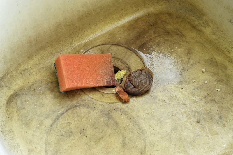 Stained and dirty unhygienic kitchen sink with wash sponge, food waste and used teabag.