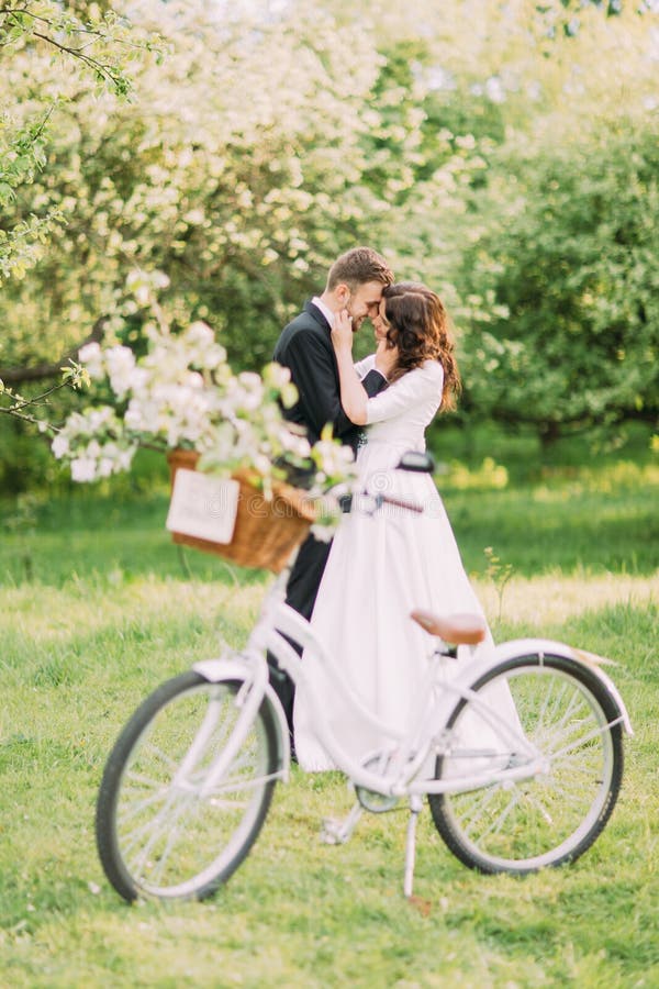 Sinnliga unga nygift personpar som rymmer sig parkerar in Cykel med bröllopgarnering på förgrund royaltyfri foto Sinnliga unga nygift personpar som rymmer sig parkerar in Cykel med bröllopgarnering på förgrund royaltyfri foto