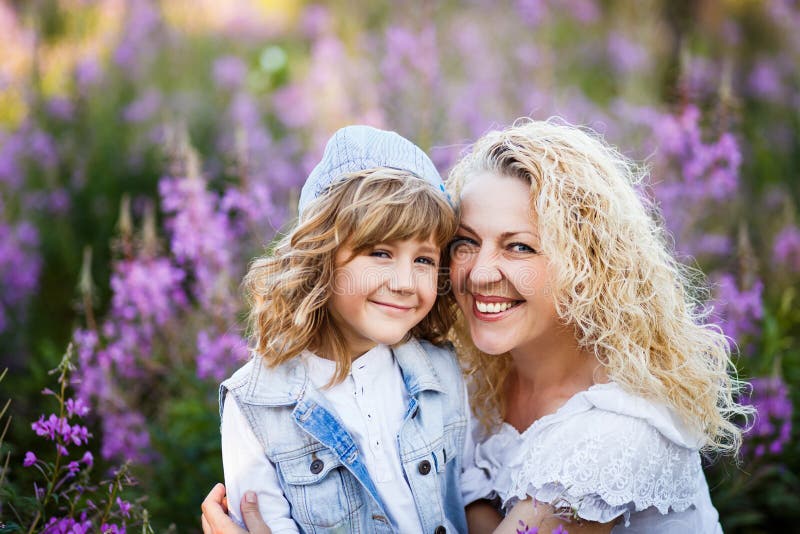 Sira de mãe e um filho pequeno bonito que abraça e que tem o divertimento no fild com as flores no verão Família e conceito da fe fotografia de stock royalty free Sira de mãe e um filho pequeno bonito que abraça e que tem o divertimento no fild com as flores no verão Família e conceito da fe fotografia de stock royalty free