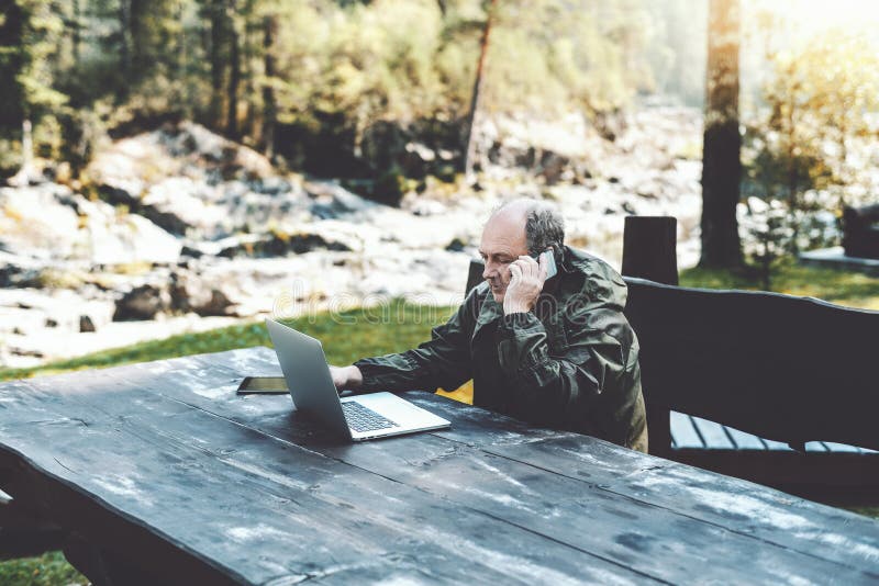Sirva al empresario con el ordenador portátil que habla en el teléfono en bosque foto de archivo Sirva al empresario con el ordenador portátil que habla en el teléfono en bosque foto de archivo