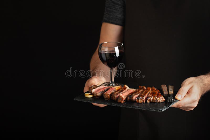 Sirva sostener el filete de carne de vaca asado a la parrilla jugoso con las especias y la copa de vino roja en una tabla de cort imagenes de archivo Sirva sostener el filete de carne de vaca asado a la parrilla jugoso con las especias y la copa de vino roja en una tabla de cort imagenes de archivo