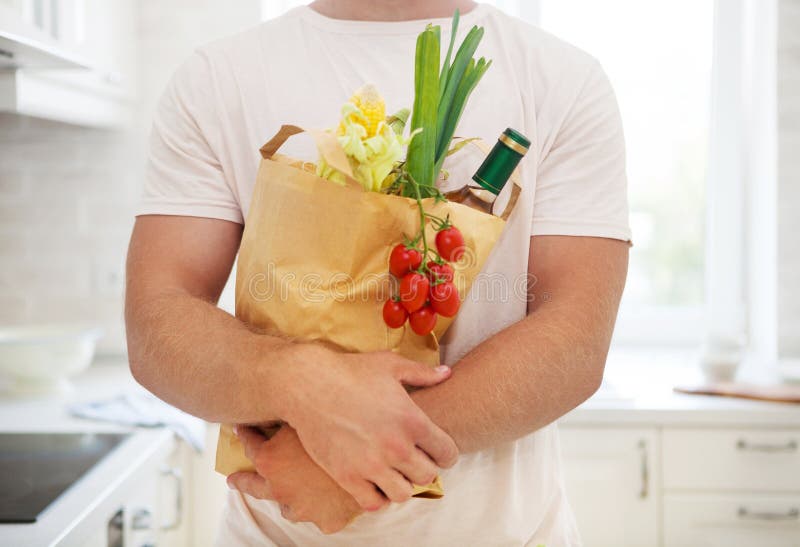 Sirva sostener la bolsa de papel llena de ultramarinos en la cocina fotos de archivo libres de regalías Sirva sostener la bolsa de papel llena de ultramarinos en la cocina fotos de archivo libres de regalías