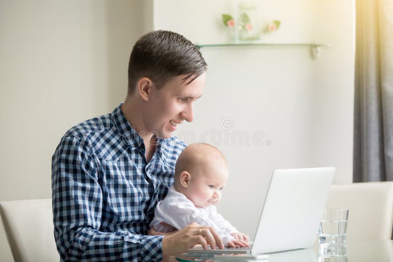 Young men working at desk at home with laptop, holding cute baby at knees, looking at screen, enjoying educational game, electronic babysitter, little helper, benefits of freelancing, safe computers. Young men working at desk at home with laptop, holding cute baby at knees, looking at screen, enjoying educational game, electronic babysitter, little helper, benefits of freelancing, safe computers