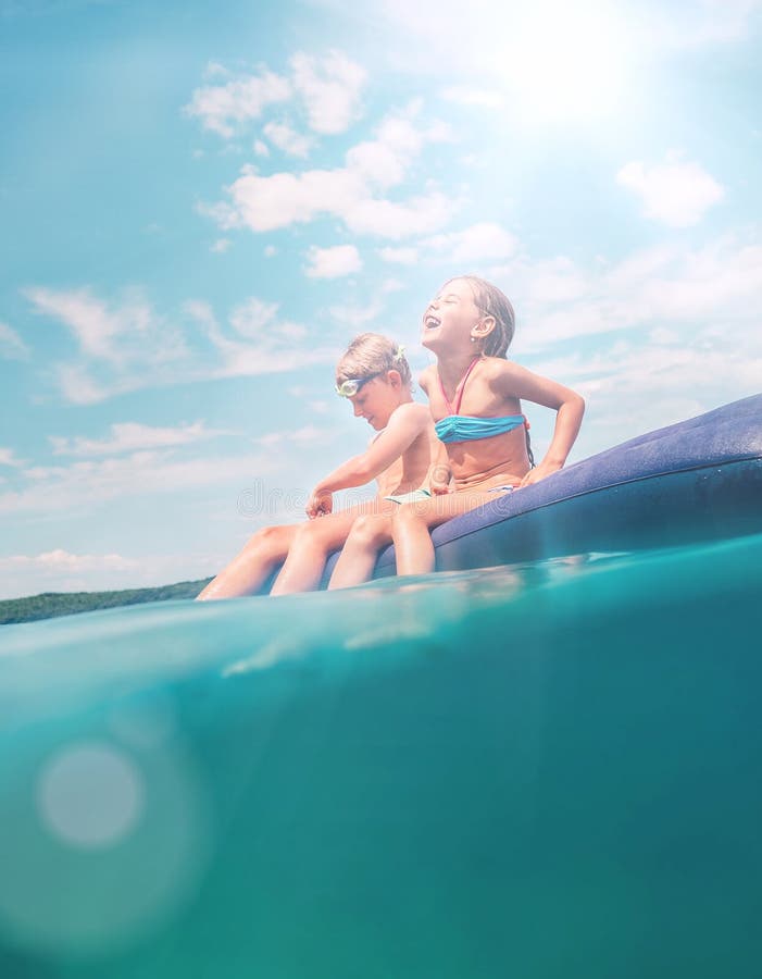 Sister and brother sitting on inflatable mattress and enjoying the sea water, cheerfully laughing when swim in the sea. Careless