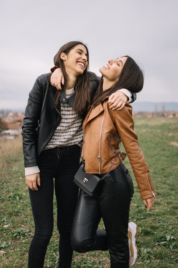 Sisters meeting and hugging in the park. Two smiling girls cuddling and enjoying spring weather while standing on field.