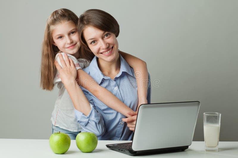 Sisters at the table with a laptop, milk and apple stock photo