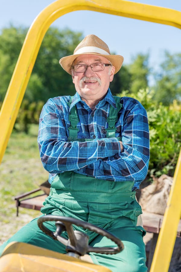 Sitta för hög man som är stolt i hans traktor, når att ha odlat hans lantgård royaltyfri fotografi Sitta för hög man som är stolt i hans traktor, når att ha odlat hans lantgård royaltyfri fotografi