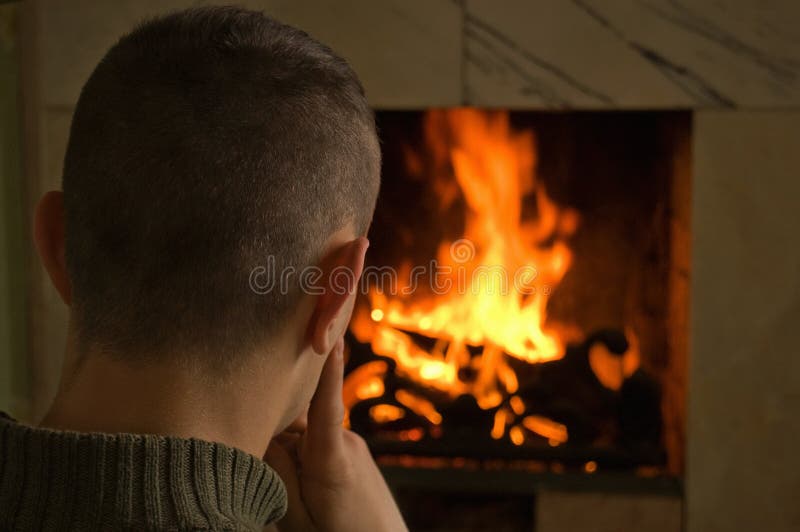 Young man sitting comfortably at marble fireplace looking at fire. Young man sitting comfortably at marble fireplace looking at fire