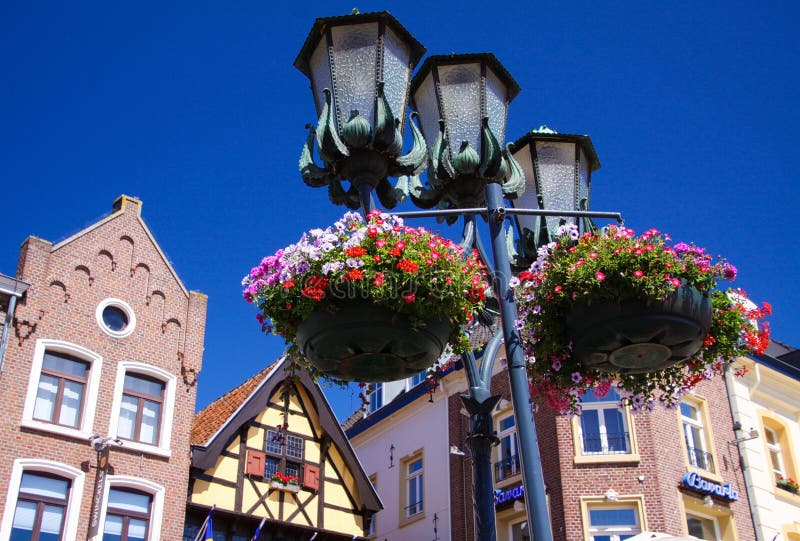 SITTARD, PAESI BASSI - JUIN 29 2019: Vista di angolo basso sulle lampade di via decorate con i canestri del fiore contro cielo bl immagini stock libere da diritti SITTARD, PAESI BASSI - JUIN 29 2019: Vista di angolo basso sulle lampade di via decorate con i canestri del fiore contro cielo bl immagini stock libere da diritti