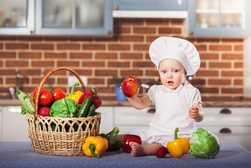 Sitter hatten och förklädet för kock för iklädd vit för liten flicka, bland vege arkivfoton Sitter hatten och förklädet för kock för iklädd vit för liten flicka, bland vege arkivfoton