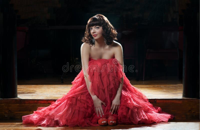 Sitting woman in red evening dress against the dark background