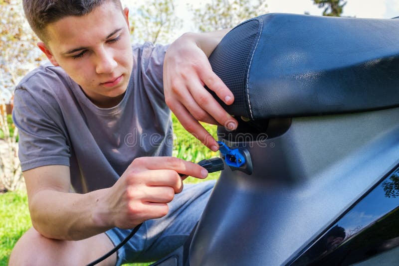 Teen inserts plug into charging socket of electric scooter. Close up view. Teen inserts plug into charging socket of electric scooter. Close up view