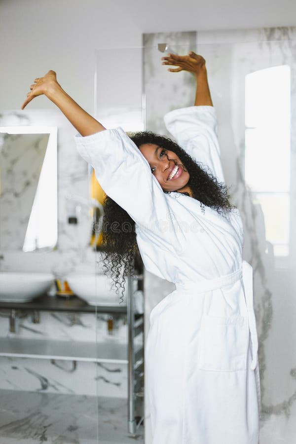 Situación afroamericana joven de la mujer en cuarto de baño y albornoz blanca que lleva fotos de archivo libres de regalías Situación afroamericana joven de la mujer en cuarto de baño y albornoz blanca que lleva fotos de archivo libres de regalías