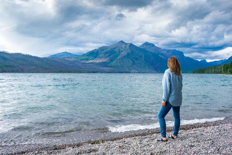 Situación de la mujer a lo largo de la orilla del lago que admira las montañas imagen de archivo Situación de la mujer a lo largo de la orilla del lago que admira las montañas imagen de archivo