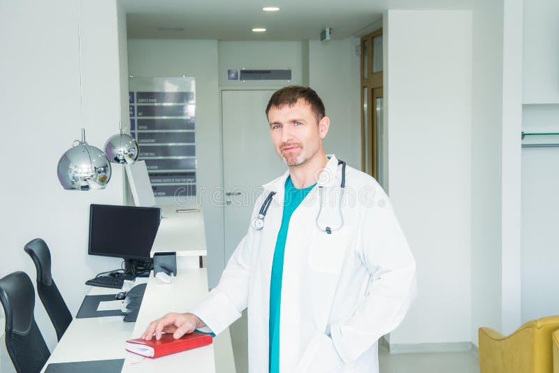 Situación del retrato del doctor confiado de sexo masculino maduro en el mostrador de recepción del hospital en el pasillo de la fotos de archivo Situación del retrato del doctor confiado de sexo masculino maduro en el mostrador de recepción del hospital en el pasillo de la fotos de archivo