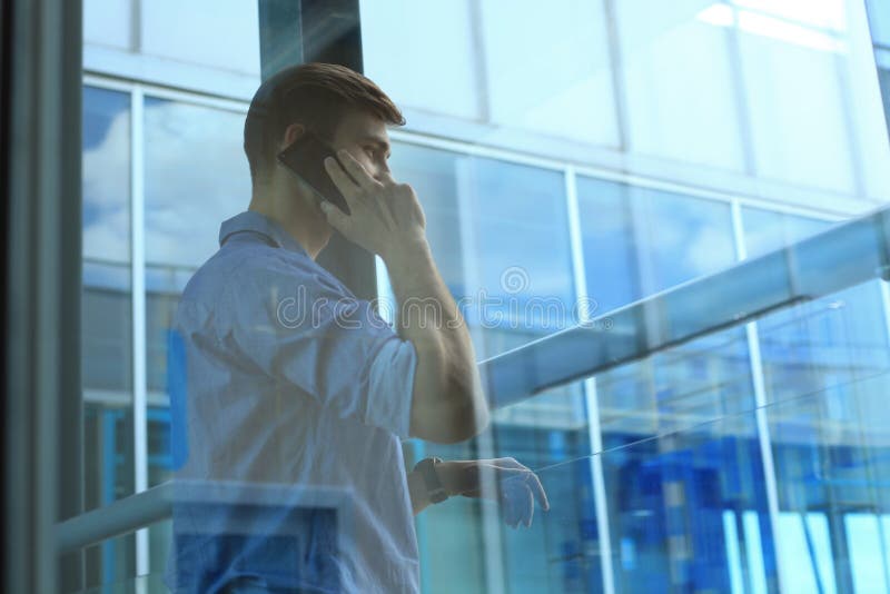 Situación y usar sonrientes del hombre de negocios el teléfono móvil en oficina imágenes de archivo libres de regalías Situación y usar sonrientes del hombre de negocios el teléfono móvil en oficina imágenes de archivo libres de regalías