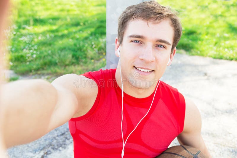 Sitzender Kerl in einem Basketballplatz und nehmen ein selfie nachdem Match mit Freunden - hört Musik mit Kopfhörern lizenzfreies stockfoto Sitzender Kerl in einem Basketballplatz und nehmen ein selfie nachdem Match mit Freunden - hört Musik mit Kopfhörern lizenzfreies stockfoto