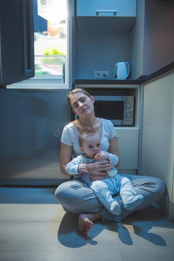 Sitzender Küchenboden der schläfrigen müden Frau an der Nacht und an der Fütterung ihres Babys mit Milch stockfotografie Sitzender Küchenboden der schläfrigen müden Frau an der Nacht und an der Fütterung ihres Babys mit Milch stockfotografie