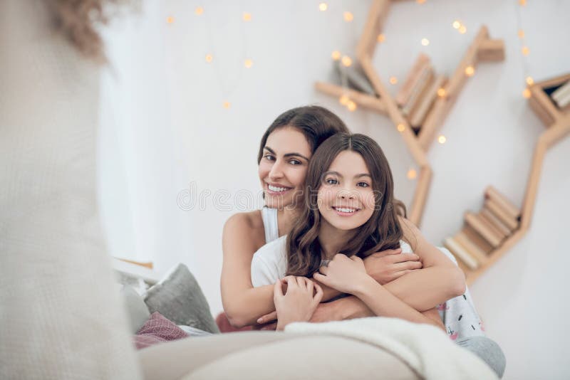 Sitzendes Umarmungen der freundlichen Teenager und vierfache Mutter und Tochter stockfoto