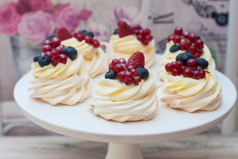 Six mini Pavlova meringue cakes with whipped cream, fresh red currant, raspberry and blueberry on white cakestand