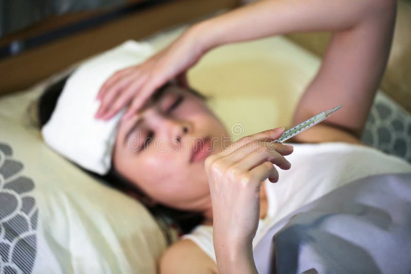 Sjuk kvinna som har en influensa med att mäta temperatur i säng royaltyfria foton Sjuk kvinna som har en influensa med att mäta temperatur i säng royaltyfria foton
