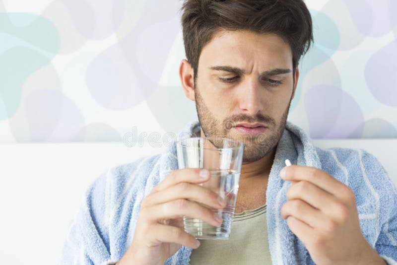 Sjuk man som hemma tar medicin i sovrum arkivfoto Sjuk man som hemma tar medicin i sovrum arkivfoto
