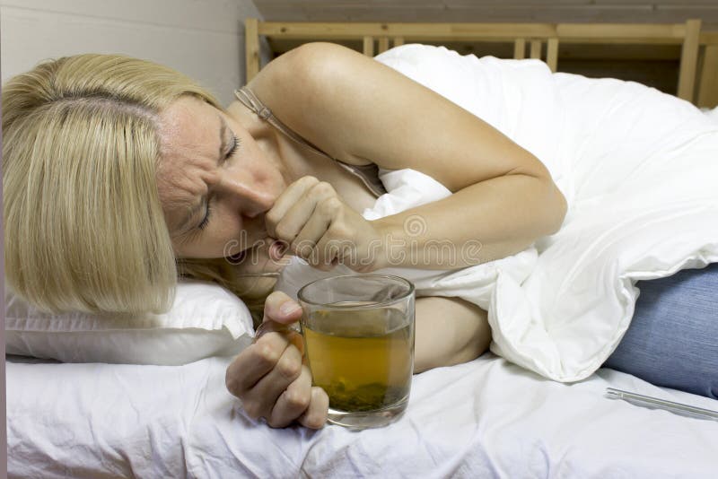 Sjuk ung blond kvinna som rymmer en kopp av grönt te och hostar på soffan arkivbild Sjuk ung blond kvinna som rymmer en kopp av grönt te och hostar på soffan arkivbild