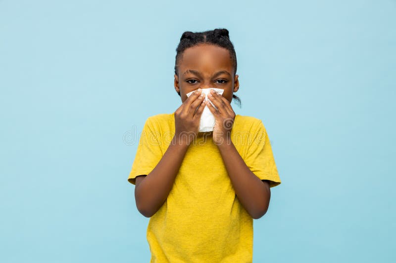 Sick dark- skinned little boy sneezing with handkerchief isolated over blue background. Sick dark- skinned little boy sneezing with handkerchief isolated over blue background