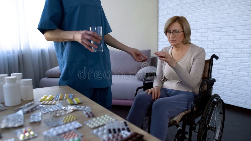 Sjukhussjuksköterska som ger preventivpillerar till den kvinnliga patienten i rullstolbehandlingrutin arkivfoto Sjukhussjuksköterska som ger preventivpillerar till den kvinnliga patienten i rullstolbehandlingrutin arkivfoto