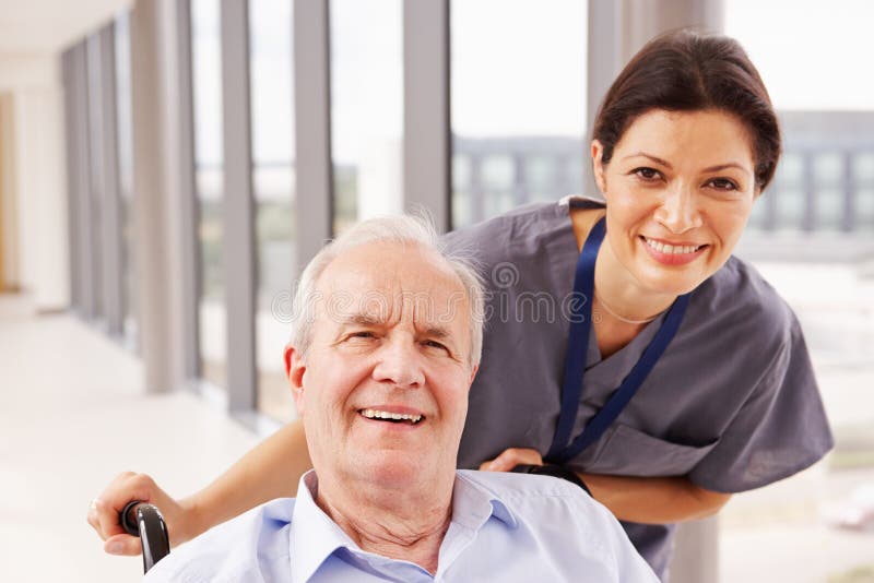 Sjuksköterska Pushing Senior Patient i rullstol längs korridoren fotografering för bildbyråer Sjuksköterska Pushing Senior Patient i rullstol längs korridoren fotografering för bildbyråer