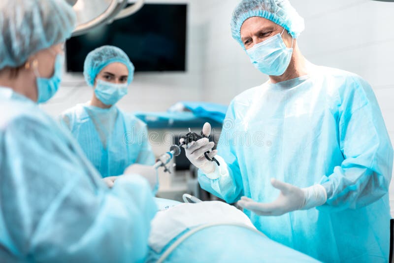 Sjuksköterska som ger det laparoscopic instrumentet för att manipulera under kirurgi royaltyfri bild Sjuksköterska som ger det laparoscopic instrumentet för att manipulera under kirurgi royaltyfri bild