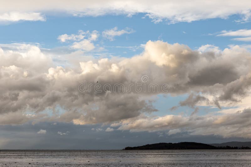 Sjö på lynnig dag med stora moln över en ö och en blå himmel royaltyfri bild Sjö på lynnig dag med stora moln över en ö och en blå himmel royaltyfri bild