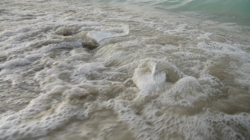 Sjövågor som rullar på sopsäckar och plastpåsar som ligger på sandstrand.. Begreppet ekologi skadar föroreningen av den smutsiga n