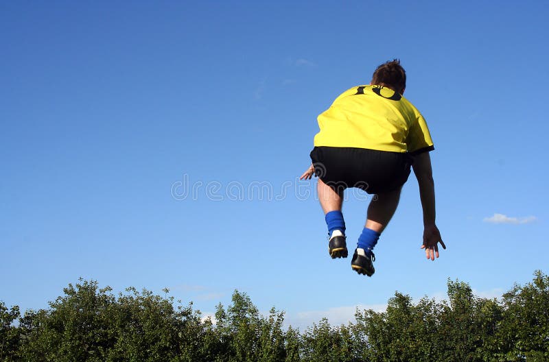 Picture of young football (soccer) player jumping high in the air, as if he's going over the trees. Picture of young football (soccer) player jumping high in the air, as if he's going over the trees.