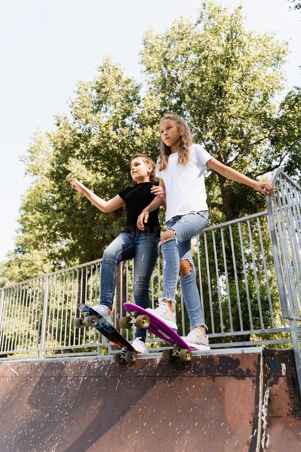 Skakare, barn flickor åker på penny board på sportramp vid solnedgången tillsammans. sportutrustning för barn royaltyfri fotografi