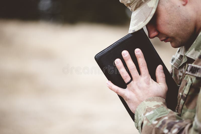 Skalbar fokus på en ung soldat som ber medan han håller bibeln