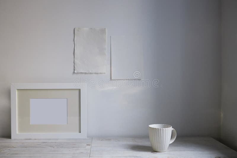 Scandinavian style. Interior Design. A white cup, , a frame for a photo are on the table. Two blank sheets of paper are attached to the wall. Empty space for text. Scandinavian style. Interior Design. A white cup, , a frame for a photo are on the table. Two blank sheets of paper are attached to the wall. Empty space for text