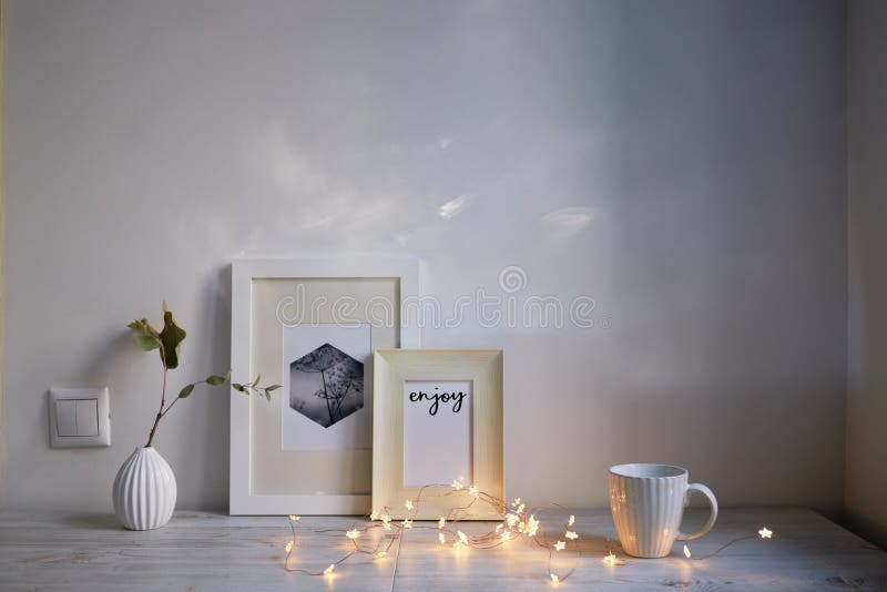 Scandinavian style. Interior Design. A white cup, cozy lights of a luminous garland, a small vase with a dried eucalyptus branch, a photo frame is on the table. Empty space for text. Scandinavian style. Interior Design. A white cup, cozy lights of a luminous garland, a small vase with a dried eucalyptus branch, a photo frame is on the table. Empty space for text