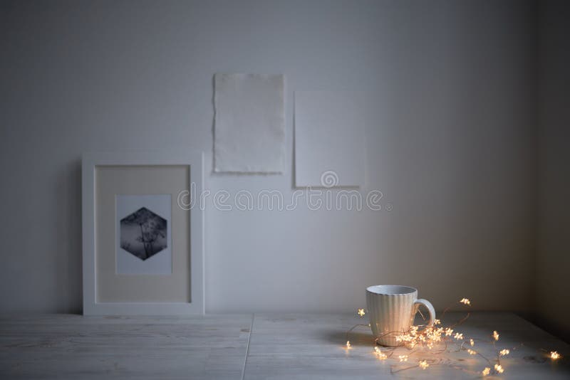 Scandinavian style. Interior Design. A white cup, cozy lights of a luminous garland, a frame for a photo are on the table. Two blank sheets of paper are attached to the wall. Empty space for text. Scandinavian style. Interior Design. A white cup, cozy lights of a luminous garland, a frame for a photo are on the table. Two blank sheets of paper are attached to the wall. Empty space for text