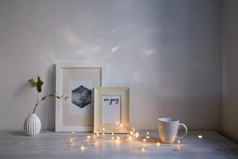 Scandinavian style. Interior Design. A white cup, cozy lights of a luminous garland, a small vase with a dried eucalyptus branch, a photo frame is on the table. Empty space for text. Scandinavian style. Interior Design. A white cup, cozy lights of a luminous garland, a small vase with a dried eucalyptus branch, a photo frame is on the table. Empty space for text