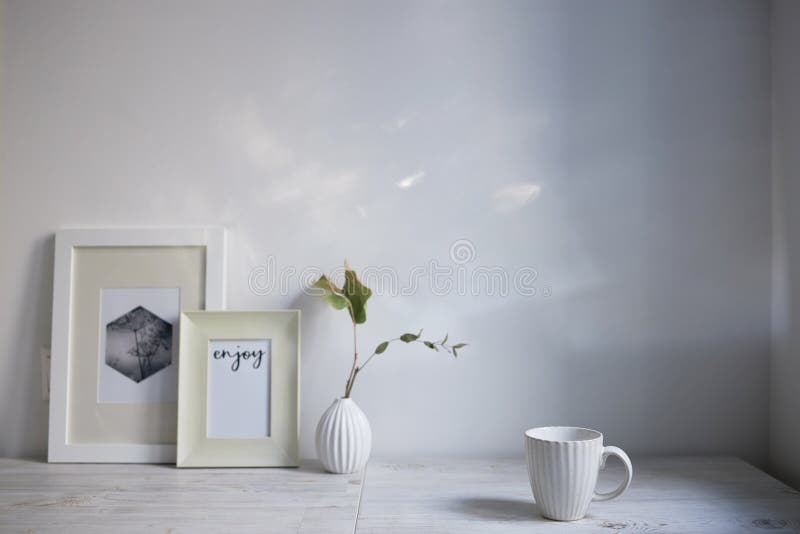 Scandinavian style. Interior Design. A white cup, a small vase with a dried eucalyptus branch, a two photo frames are on the table. Copy space for text. Scandinavian style. Interior Design. A white cup, a small vase with a dried eucalyptus branch, a two photo frames are on the table. Copy space for text