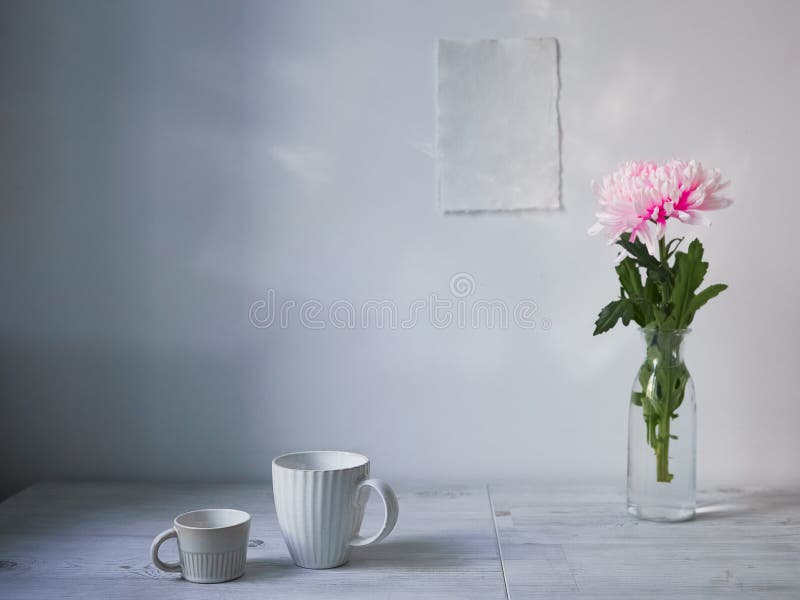Scandinavian style. Interior Design. Large pink chrysanthemum in a long glass vase. Two cups of different size. Two blank sheets of paper on the wall. Empty space for text. Scandinavian style. Interior Design. Large pink chrysanthemum in a long glass vase. Two cups of different size. Two blank sheets of paper on the wall. Empty space for text