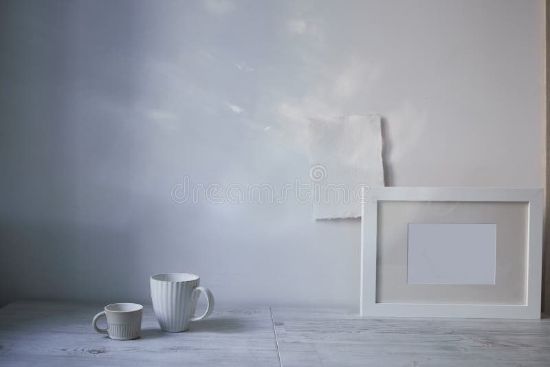 Scandinavian style. Interior Design. A white cups of different size, a frame for a photo are on the table. the blank sheets of paper are attached to the wall. Empty space for text. Scandinavian style. Interior Design. A white cups of different size, a frame for a photo are on the table. the blank sheets of paper are attached to the wall. Empty space for text