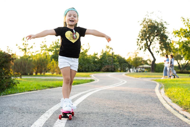 Skate da equitação da criança no parque do verão Menina que aprende montar a placa do patim Esporte exterior ativo para a escola fotografia de stock royalty free Skate da equitação da criança no parque do verão Menina que aprende montar a placa do patim Esporte exterior ativo para a escola fotografia de stock royalty free