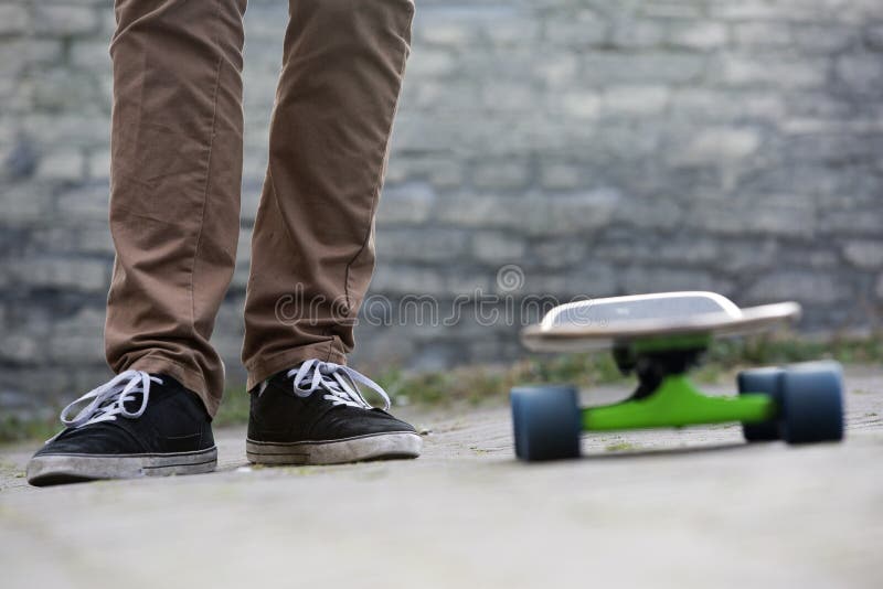 Skateboarder feet and skateboard in urban setting. The two feet of a casually dressed man standing next to a skateboard in an urban setting, with a brick wall in stock photography Skateboarder feet and skateboard in urban setting. The two feet of a casually dressed man standing next to a skateboard in an urban setting, with a brick wall in stock photography